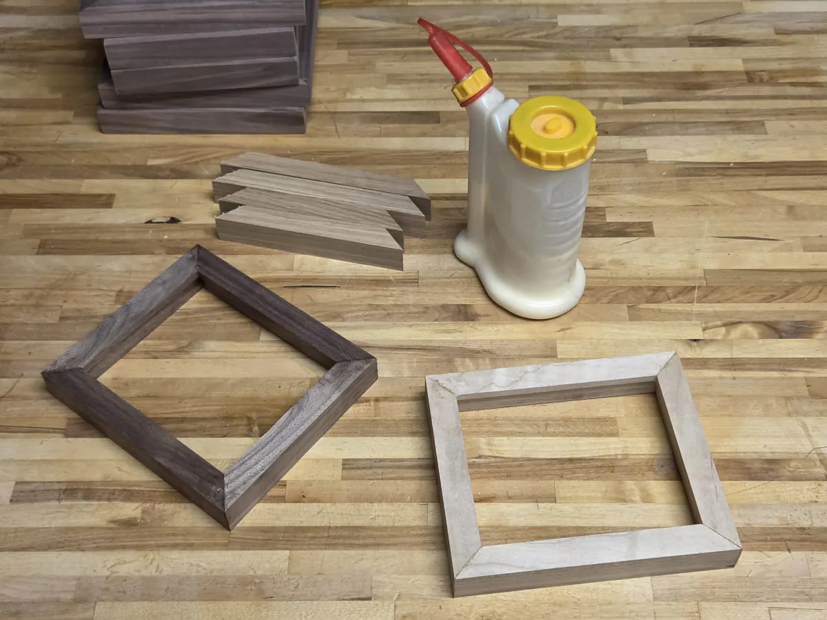 A walnut frame and a maple frame glued up beside a bottle of wood glue and a stack of offcuts