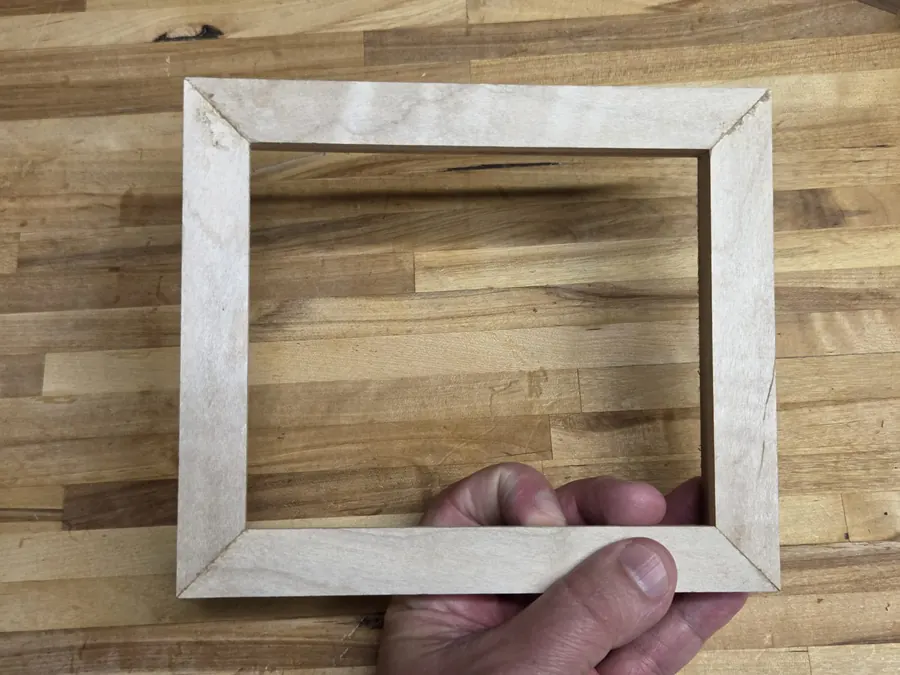 A finished maple frame held in one hand above the bench