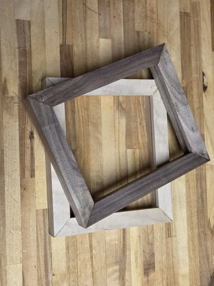 A walnut frame laid at an angle across a maple one on the workbench