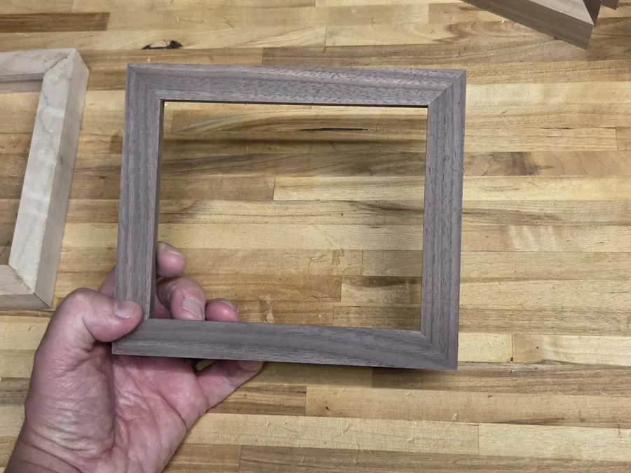 A finished walnut frame held in one hand above the bench